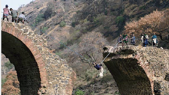 Men on either side of Blue Nile River in Ethiopia pull each other across the broken bridge by a rope